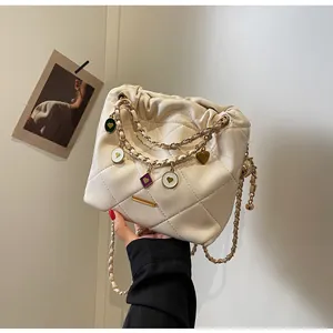 Gros plan du sac seau matelassé beige avec chaîne dorée et breloques en forme de cœur