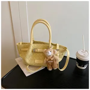 Détail du sac seau jaune clair tressé avec breloque d'ours et logo Chermate gravé