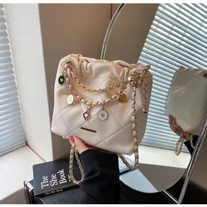 Détail d'un sac seau matelassé beige avec chaîne dorée et pendentifs en forme de cœur