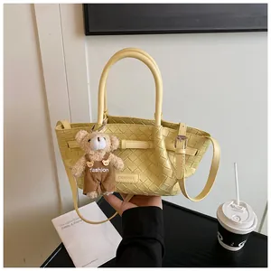 Détail d'un sac seau tressé jaune clair avec breloque d'ours et logo de marque