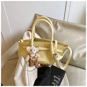 Détail d'un sac seau tissé jaune clair avec breloque ours en peluche et anses rondes