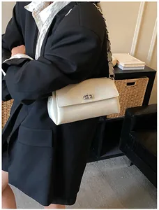 Détail d'un sac sous le bras blanc crème avec fermoir rotatif argenté et bandoulière chaîne