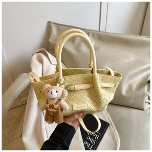 Détail d'un sac seau jaune clair tressé avec breloque ours sur fond de blazer blanc