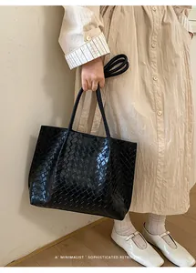 Détail d'un sac cabas noir tressé minimaliste porté à l'épaule par un mannequin