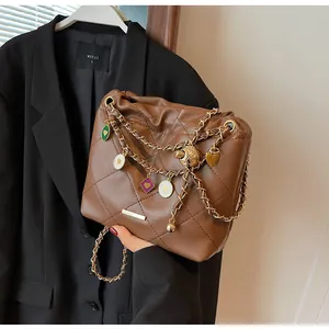 Détail d'un sac seau marron matelassé avec chaîne dorée et breloques cœur sur tissu noir