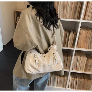 Detail einer cremeweißen Lackleder-Hobo-Tasche mit dekorativen Nieten und Reißverschlüssen