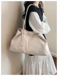 Detail of a large cream glossy tote bag worn by a model in a minimalist setting