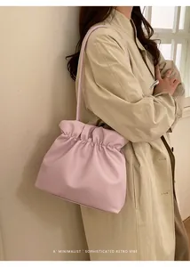 Minimalist soft pink gathered bucket bag shown as a shoulder bag on a model in a trench coat