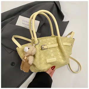 Détail du sac seau tissé jaune clair avec breloque ours sur un blazer gris chic