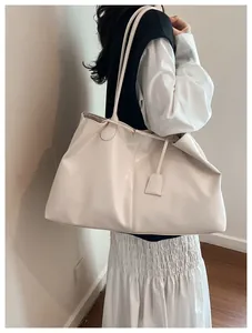 Close-up of a large cream tote bag showing glossy leather texture and stylish side charm