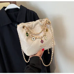 Détail du sac seau matelassé crème avec chaîne dorée et breloques de cœur