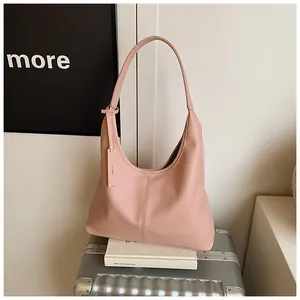 Sac fourre-tout en cuir grainé rose posé sur une valise dans un décor minimaliste moderne