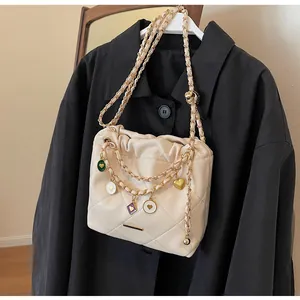 Détail du sac seau matelassé beige avec breloques coeur dorées et bandoulière en chaîne