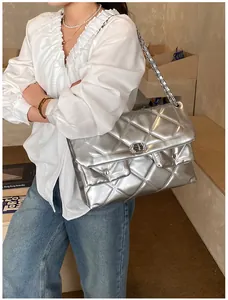 Detail of silver quilted handbag with metal chain strap worn by model in casual outfit