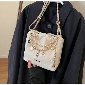 Détail du sac seau matelassé beige avec breloques cœur et bandoulières en chaîne dorée