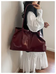 Detail of dark burgundy glossy tote bag shown worn by a model in a modern interior