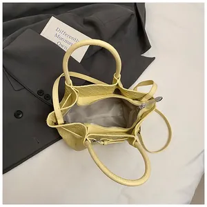 Détail du sac seau jaune tressé montrant le compartiment zippé et la bandoulière