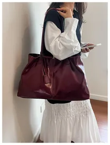 Detail of burgundy large tote bag in glossy patent leather finish on female model