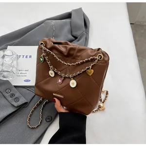 Détails d'un sac seau matelassé marron avec chaîne dorée et breloques en cœur