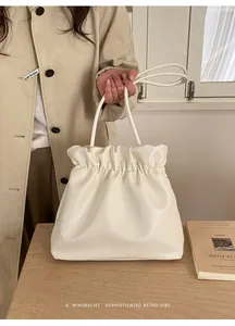 Detail of minimalist cream leather bucket bag with elegant pleats and long handles