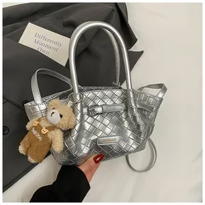 Détail du sac seau tressé argenté avec plaque logo en métal et pendentif ours mignon
