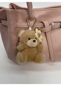 Detailed view of a brown plush bear charm with a yellow flower on a pink leather handbag