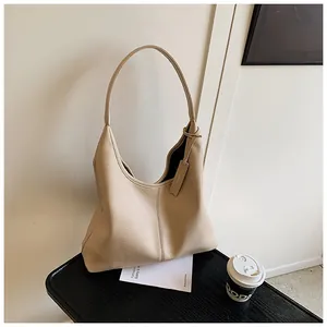 Gros plan du sac hobo en cuir beige texturé litchi sur une table avec un café