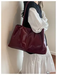 Detail of burgundy large capacity tote bag with glossy finish shown on model shoulder