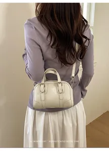 Modella che indossa una mini borsa Boston bianco crema con fibbie retrò e tracolla