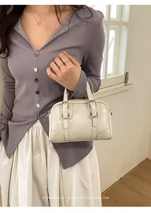 Dettaglio di una mini borsa Boston in pelle verniciata bianca con fibbie metalliche