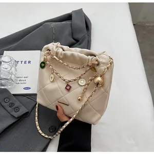 Détail du sac seau matelassé crème avec chaîne dorée et breloques en cœur