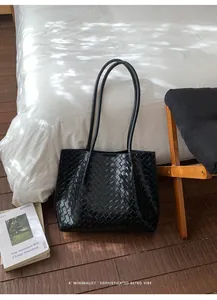Détail d'un sac cabas noir en cuir tressé avec de longues anses sur un sol minimaliste
