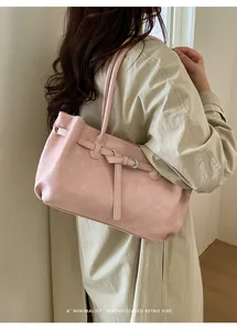 Minimalist pink soft leather tote bag with silver buckle worn by a model in a warm room