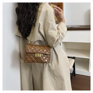 Détail d'un sac à main en cuir verni marron foncé avec fermoir doré et bandoulière en chaîne