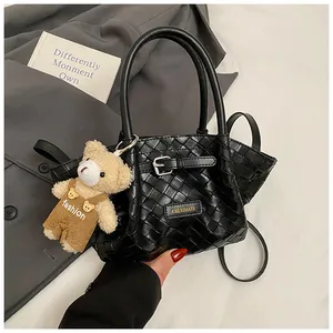 Détail d'un sac seau tressé noir avec logo métallique et charmant ours en peluche