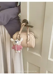 Dettaglio di una borsa Boston beige con cinturino a fibbia e ciondolo orsetto morbido