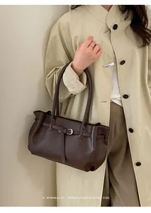 Detail of dark brown leather tote bag with vintage buckle strap on beige trench coat