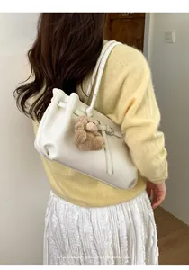 Detail of minimalist cream leather tote bag with brown plush bear charm and thin strap