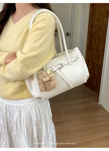 Close-up of beige leather tote with retro buckle strap and plush bear charm on handle