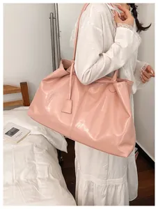 Pink glossy leather tote bag shown on shoulder of model in white lace dress