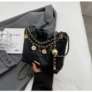 Détail du sac seau noir matelassé avec des chaînes dorées et des pendentifs en cœur