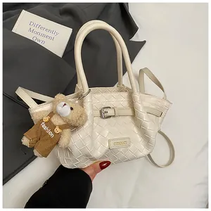 Détail d'un sac seau blanc tressé avec boucle métallique et charmant pendentif ours