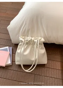 Detail of cream white pleated bucket bag with soft drawstring texture on wood floor
