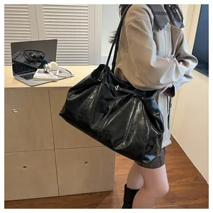 Detail of a large black leather tote bag with glossy finish and thin shoulder straps