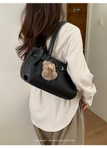 Detail view of a black soft leather tote bag with a cute brown plush bear charm