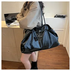 Close-up of black glossy patent leather tote bag with silver buckle and shoulder straps