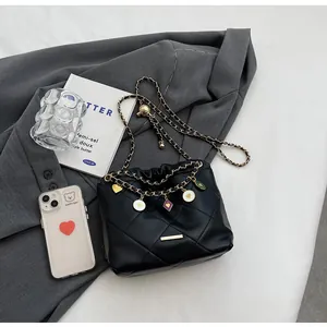 Détail du sac seau noir matelassé avec chaîne dorée et breloques en forme de cœur