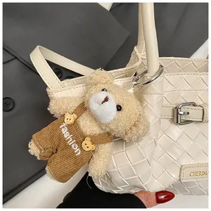 Détail du sac seau blanc tressé avec un ours en peluche marron sur tissu gris