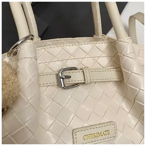 Détail d'un sac seau crème tressé avec boucle en métal argenté et écusson de marque en cuir