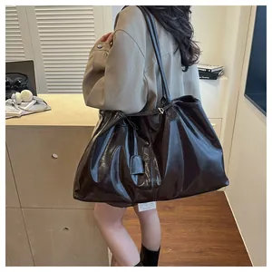Detail of a large glossy leather tote bag with long straps worn on the shoulder in a lifestyle setting